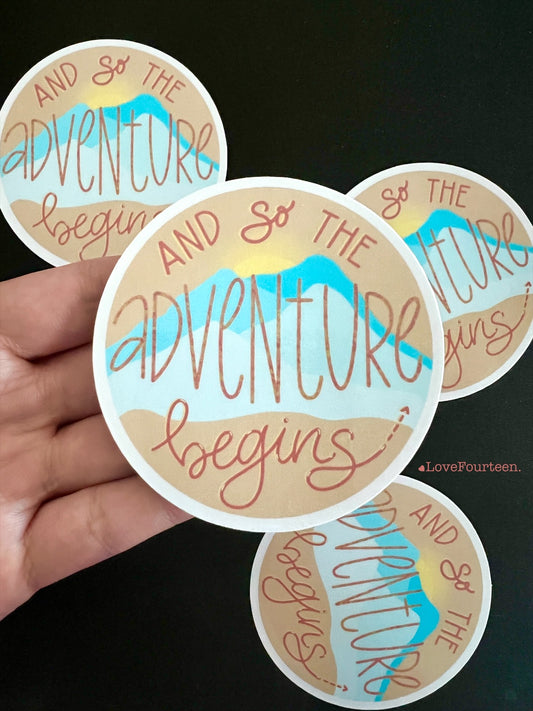 Circle waterproof die cut vinyl sticker with a saying, and so the adventure begins 
